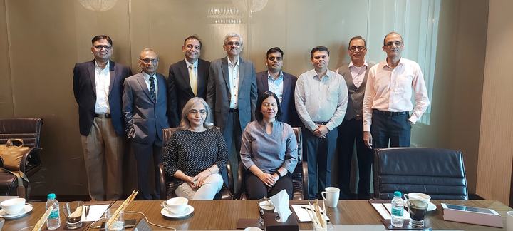 A group of about fourteen professionals, some seated and some standing, pose together in a meeting room.