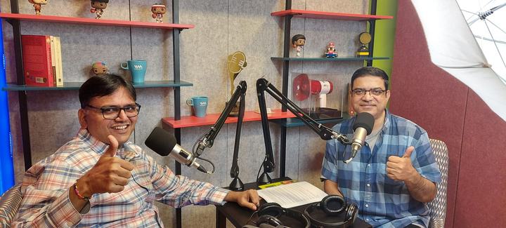 Rohit Shah and podcast host Anupam Gupta at microphones in the Paisa Vaisa podcast studio, giving a thumbs-up.