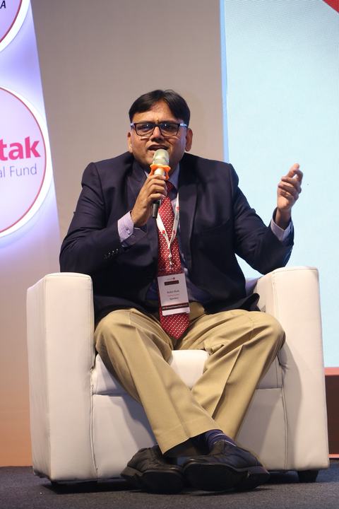 Rohit Shah, seated on stage with a microphone, speaking on a panel.