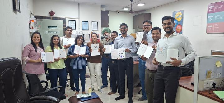 About a dozen members of the GYR team stand together in the office after a journaling session, smiling and holding open notebooks filled with drawings and notes. Posters of the firm’s vision, mission and values hang on the wall.