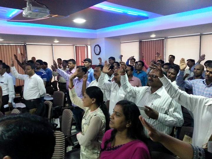Participants in a training room raise their hands in response to a question.