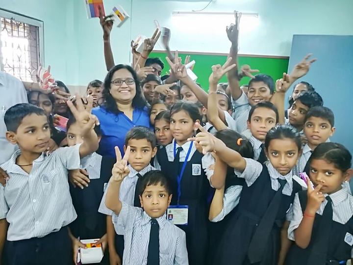 A presenter surrounded by cheerful young students making victory signs.
