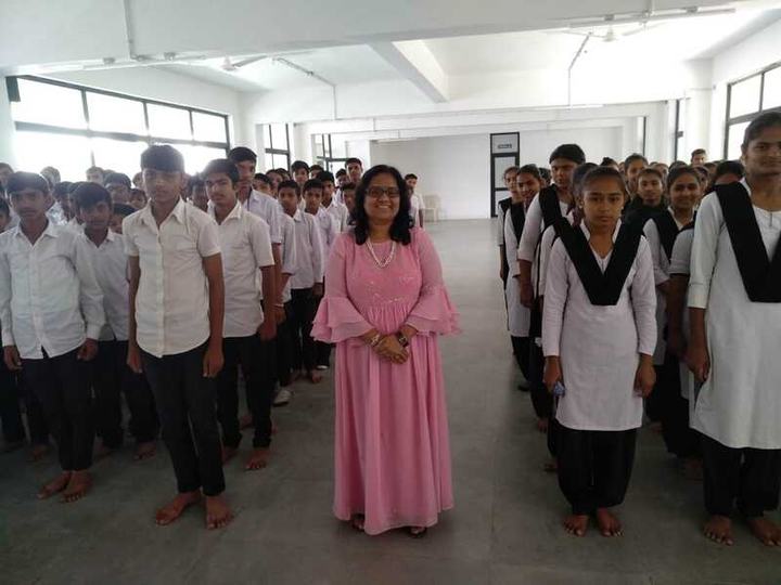A presenter stands with rows of school students in uniform in a large hall.