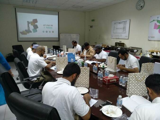 Participants at a conference table, with a presentation on a screen behind them.