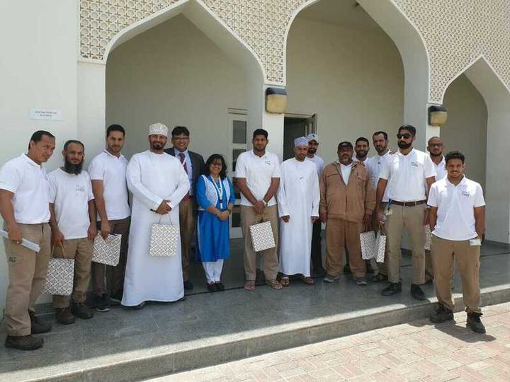 A group of participants, several in traditional Omani dress, stand outside a building with arched doorways.