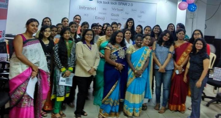 A large group of women, many in saris, stand together in an office.