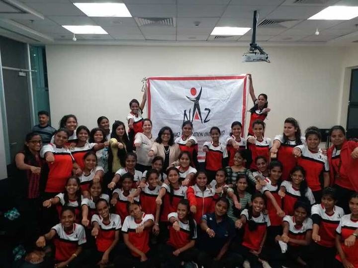 A large group of girls in red sports uniforms in front of a Naz Foundation banner.