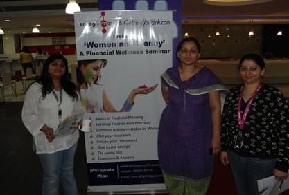 Three women stand beside a banner reading ‘Women and Money: a financial wellness seminar’.