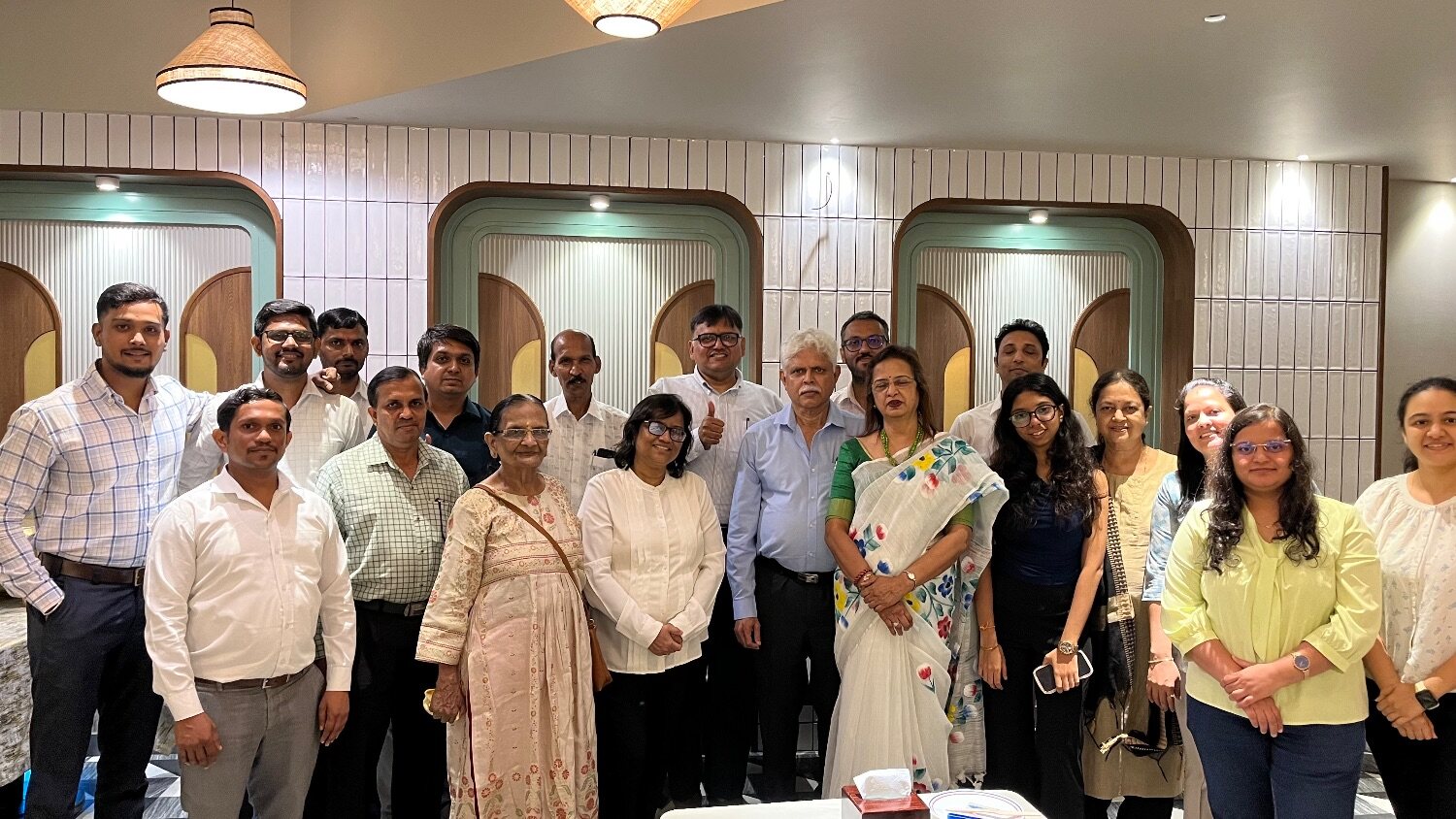 About twenty members of the GYR and VSK teams stand together in two rows in a restaurant with arched alcoves and pendant lamps, smiling at the camera; one person at the back gives a thumbs-up.